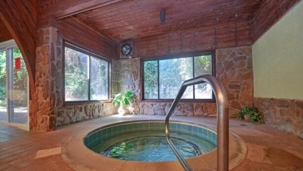 A hot tub with a stone wall and wooden ceiling, surrounded by windows.