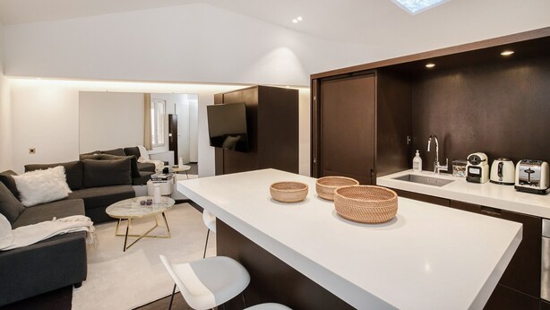 A modern living space with a sofa, coffee table, and a kitchen area with a sink and appliances. - Appartement Place des lices Avec Parking (Saint-Tropez)