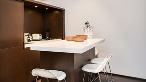 A modern kitchen with a white countertop, three white bar stools, and a small island with baskets and a card holder. - Appartement Place des lices Avec Parking (Saint-Tropez)