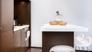 A modern kitchen with dark wood cabinets, a white countertop, and a small dining area with white chairs. - Appartement Place des lices Avec Parking (Saint-Tropez)