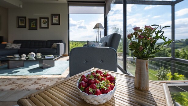 Ett modernt vardagsrum med en soffa, ett soffbord med en skål med jordgubbar och en vas med blommor.