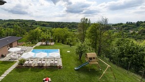 En trädgård med en pool, solstolar, ett litet trähus för lek och en rutschkana.