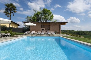 A swimming pool with lounge chairs and umbrellas, a brick building with a chimney, and a view of a green landscape. - Private Villa with A/C, WIFI, private pool, TV, patio, pets allowed, panoramic view, close to Alba (San Grato)