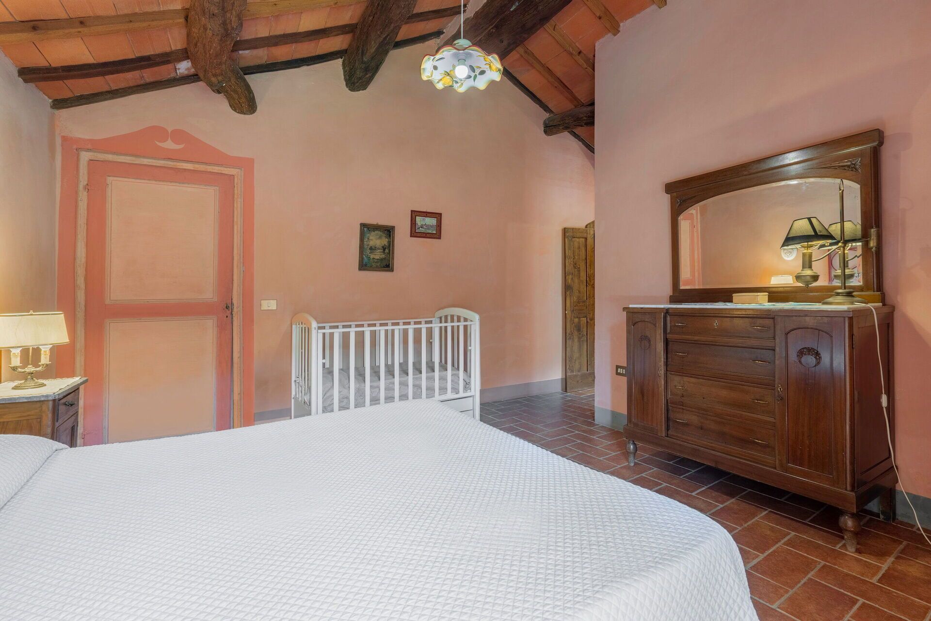 A bedroom with a bed, a wooden dresser, a mirror, and a crib.