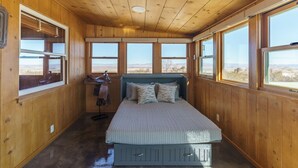 A wooden cabin room with a bed, large windows, and a view of the desert.