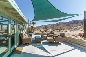 A covered outdoor seating area with wicker furniture, a pool, and a view of desert landscape.