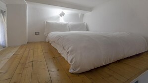 A bedroom with a wooden floor, white walls, and a bed with white bedding. - Casa Maril nel Centro Storico di Rapallo by Wonderful Italy (Rapallo)
