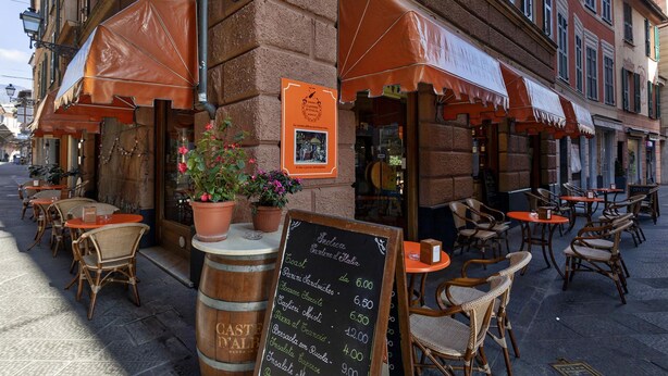 An outdoor cafe with wicker chairs and tables, a chalkboard menu, and a brick building facade. - Casa Maril nel Centro Storico di Rapallo by Wonderful Italy (Rapallo)
