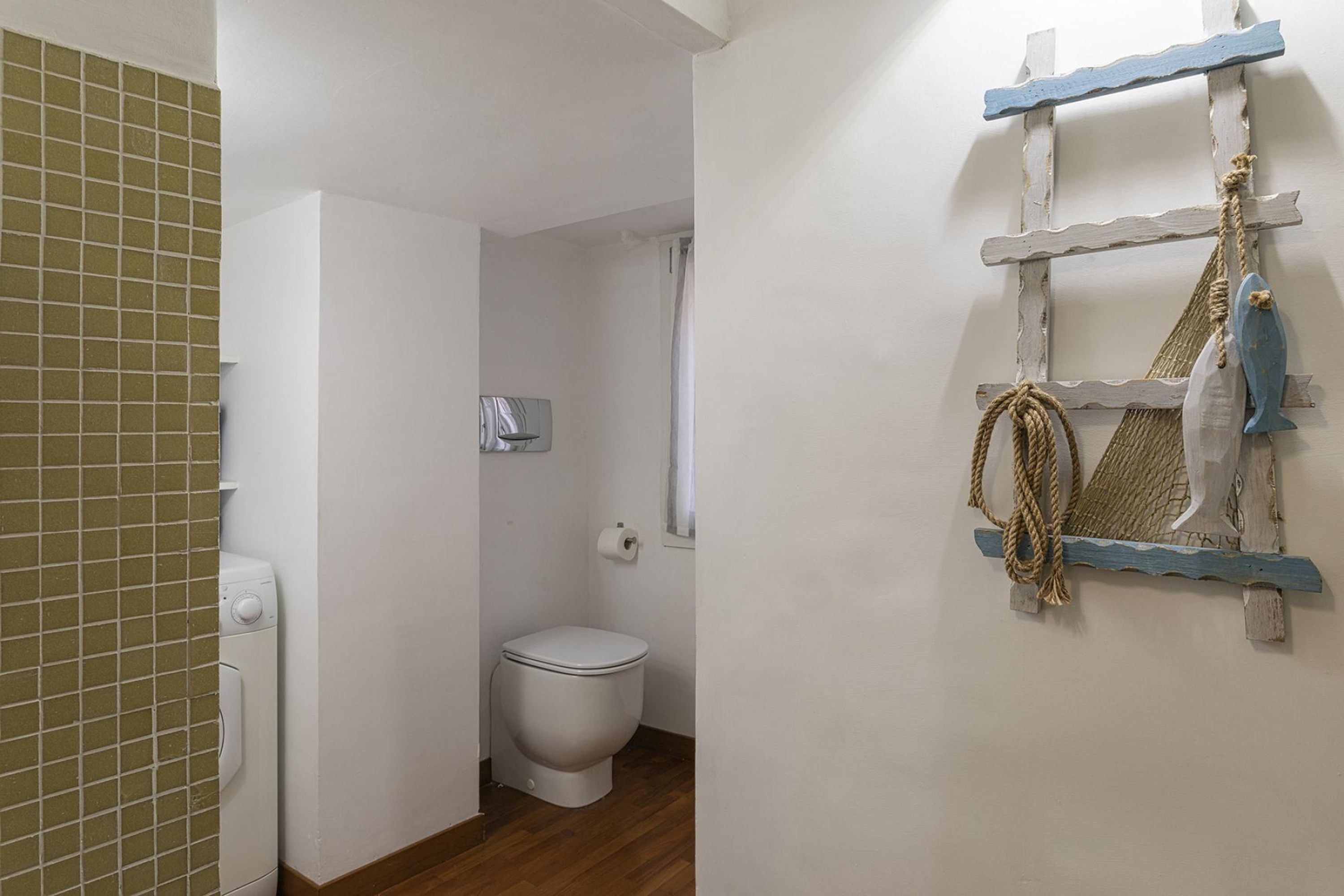 A bathroom with a white toilet, a washing machine, and a wooden floor.