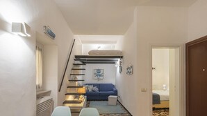A narrow hallway with a staircase leading to a loft bedroom. The room features a blue sofa, a small table with a lamp, and a bed with a white headboard. - Casa Maril nel Centro Storico di Rapallo by Wonderful Italy (Rapallo)