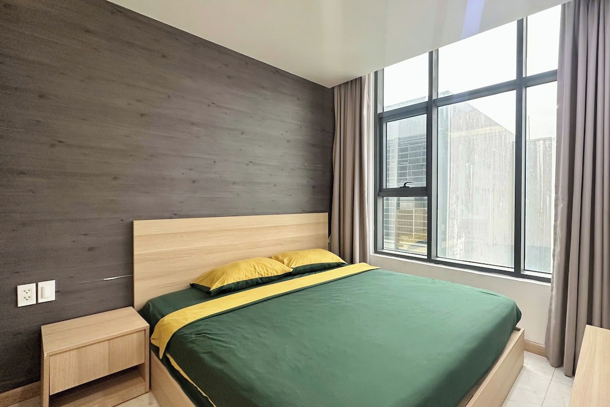 A modern bedroom with a large window, a bed with green and yellow bedding, and a dark wooden wall.