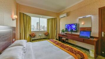 Habitación de hotel con cama, escritorio con computadora portátil, televisión y vista a un paisaje urbano a través de una ventana.