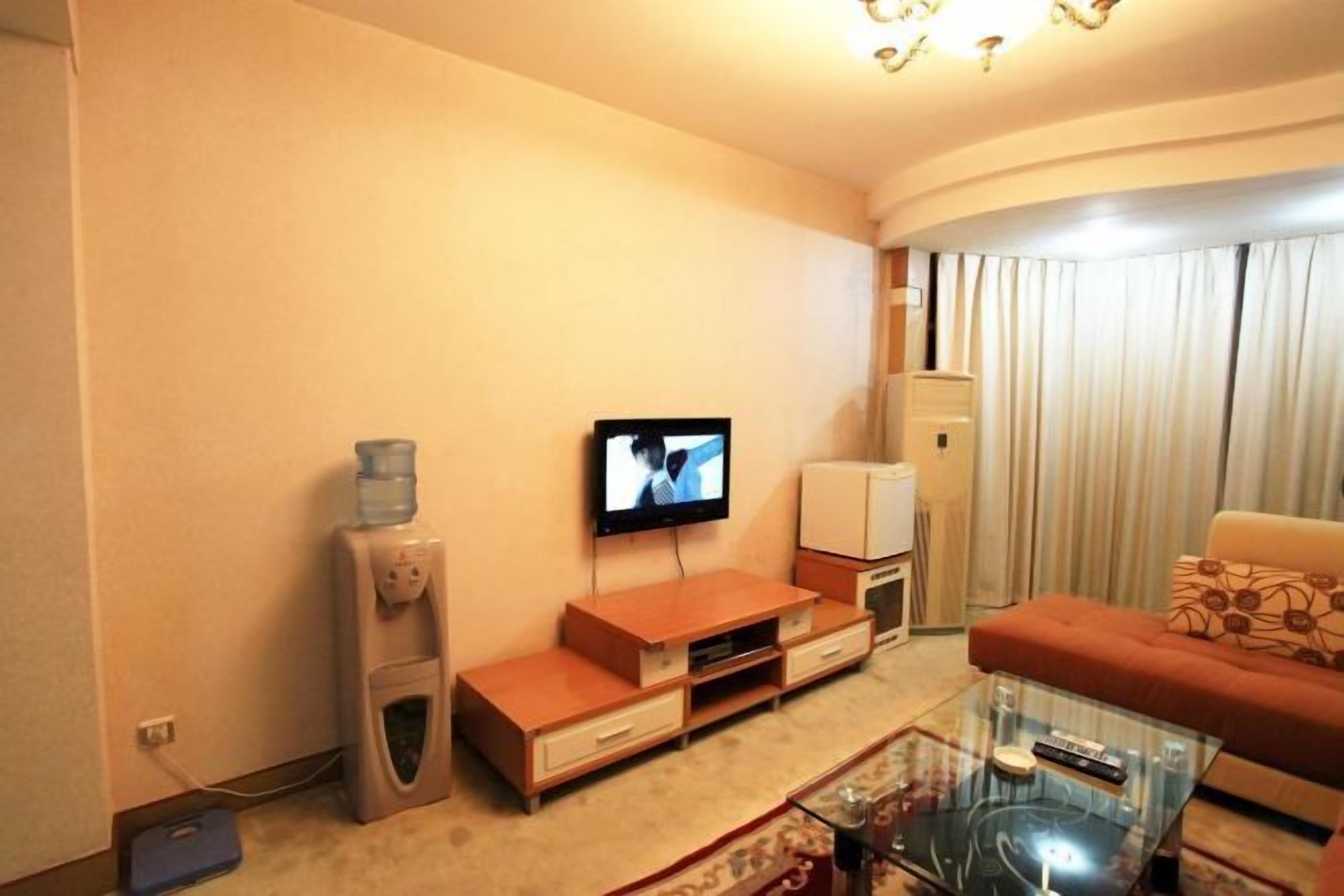 A living room with a flat-screen TV, wooden furniture, a glass coffee table, and a water dispenser.