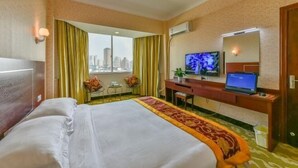 Une chambre d’hôtel avec un grand lit, un bureau avec un ordinateur portable, une télévision et une vue sur le paysage urbain.