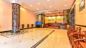 Un vestíbulo de hotel con mostrador de recepción, zona de estar y columnas decorativas.