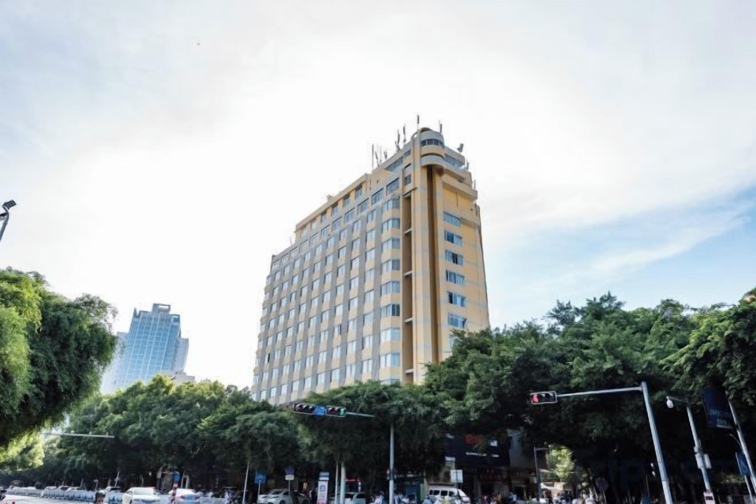 Un hotel de varios pisos en una esquina, rodeado de árboles y otros edificios.