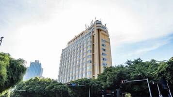 Un hotel de varios pisos en una esquina, rodeado de árboles y otros edificios.