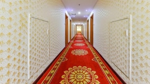 Un long couloir étroit, avec un papier peint à motifs et une moquette rouge ornée de dessins dorés.