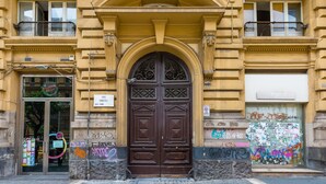 Un immeuble doté d’une grande porte marron richement décorée, d’un balcon et d’une fenêtre sur laquelle est apposée une enseigne.