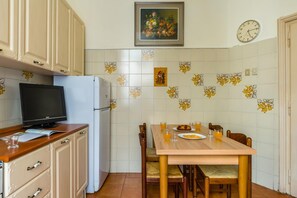 Une cuisine équipée d’un réfrigérateur, d’une télévision, d’une table à manger avec des chaises et d’une horloge murale.