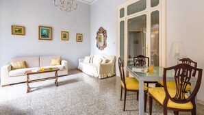 Un salon comprenant un canapé, une table à manger avec des chaises, un lustre et des tableaux encadrés accrochés au mur.