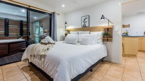 A modern bedroom with a large bed, a wooden bench, a small table, and a view of a balcony.