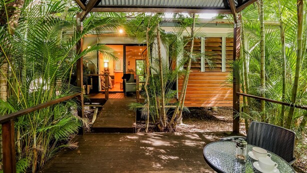 A tropical resort with a wooden deck leading to a covered area with a table and chairs.