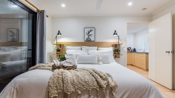 Une chambre moderne avec un grand lit, des lampes de chevet, une tête de lit en bois et une vue sur la pièce adjacente.