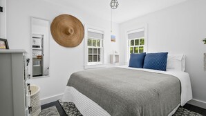 Un dormitorio con cama, un tapiz grande tejido en la pared, una lámpara colgante y un ventanal con vistas a la vegetación.