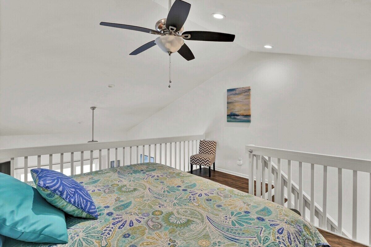 A bedroom with a bed, a chair, a ceiling fan, and a painting on the wall.