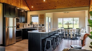 A modern kitchen with a central island, stainless steel appliances, and a dining area with a view. - Cedar Mountain Retreat- Hot Tub, Pet Friendly, Mountain Views (Cody)