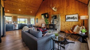 A spacious living area with a fireplace, a sofa, and a dining area with a kitchen in the background. - Cedar Mountain Retreat- Hot Tub, Pet Friendly, Mountain Views (Cody)