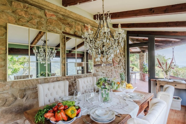 Comedor con pared de piedra, vigas de madera, candelabro y mesa preparada para una comida.