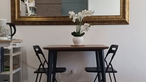 A dining area with a table and chairs, a white vase with flowers, and a large mirror with a gold frame.