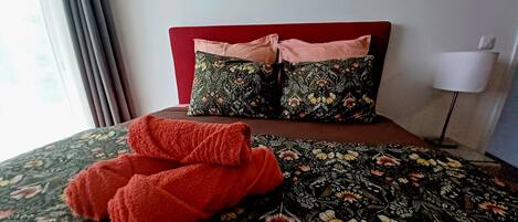 Uma cama com um edredom floral, duas almofadas e um par de toalhas vermelhas.
