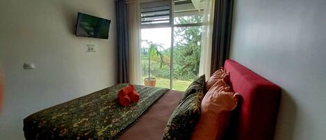 A bedroom with a bed, a ceiling fan, a window with curtains, and a television on the wall.