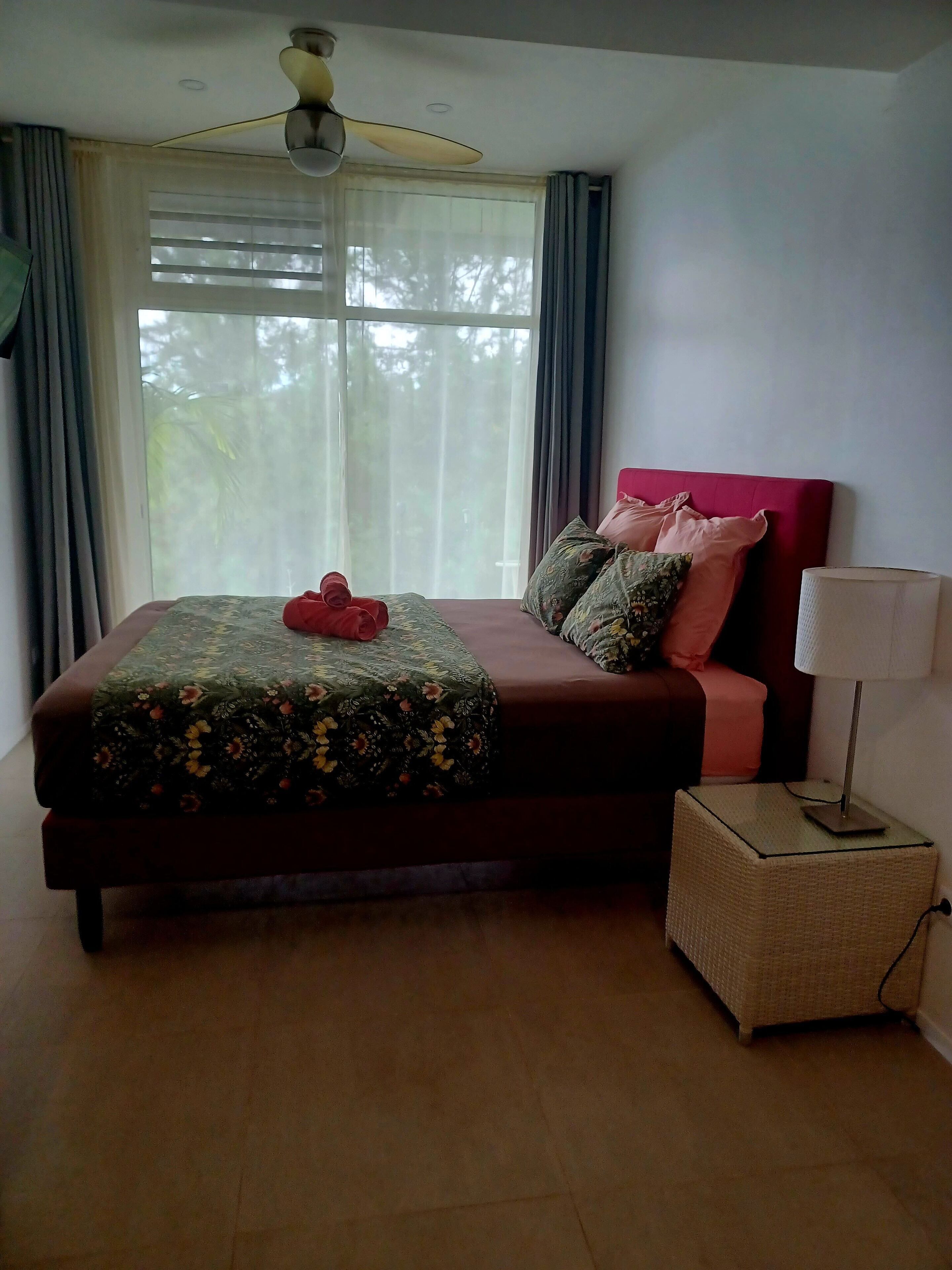Een slaapkamer met een bed, een bedlampje en een raam met gordijnen.