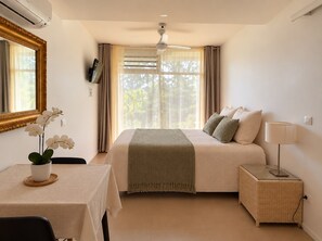 Habitación de hotel con cama, mesita de noche, lámpara y ventana con cortinas.