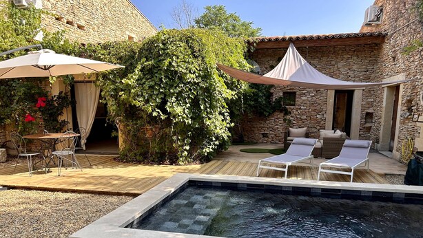 A pool area with a lounge chair, a table with chairs, and a covered seating area.