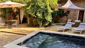 A swimming pool with a stone border, surrounded by a patio area with outdoor furniture and umbrellas.