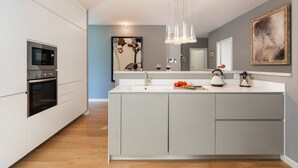 A modern kitchen with white cabinetry, a central island, a built-in oven, and a pendant light. - Luxury Marignana By Geco Vacation Rentals (Camaiore)