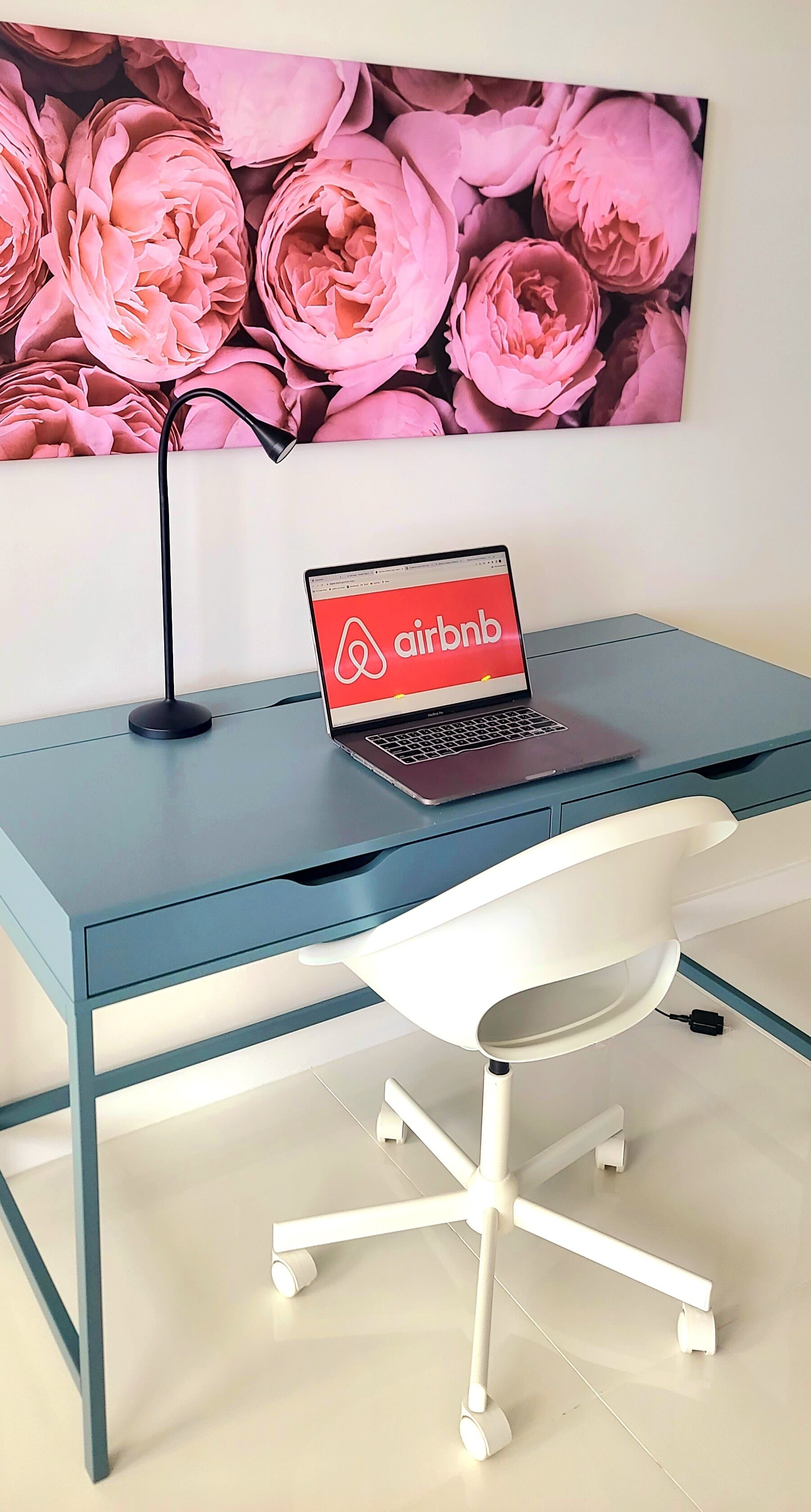 A modern desk with a laptop displaying the Airbnb logo, a white office chair, and a wall-mounted lamp.