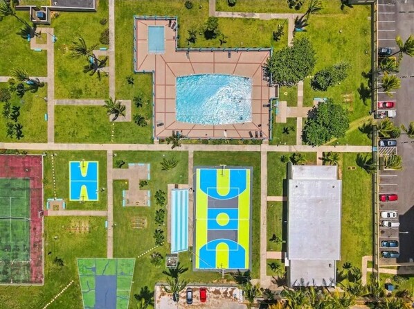 Vue aérienne d’un complexe sportif comprenant plusieurs terrains de sport, une piscine et des aires de stationnement.