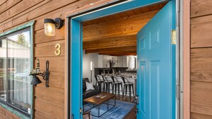 Eine Holzhütte mit blauer Tür, einer Küche mit Barhocker und einer kleinen Sitzecke.