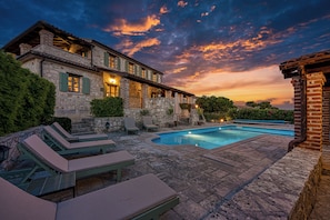 A stone building with a swimming pool, lounge chairs, and a sunset view. - Villa Amyra With Pool (Sveti Lovrec)