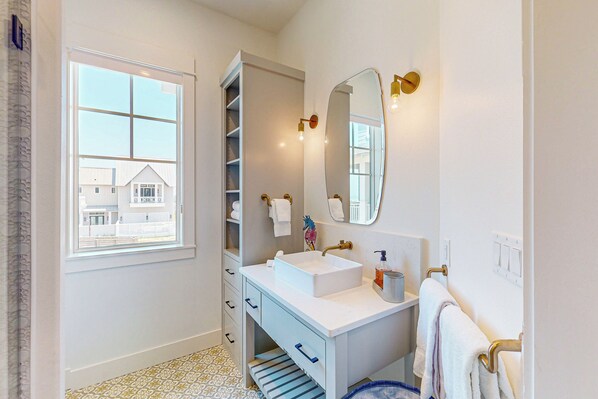 Bagno con mobile lavabo bianco, uno specchio grande e una finestra con vista sugli edifici.