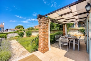 Een terras met een tafel en stoelen, een bakstenen pilaar en een pergola.
