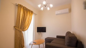 A living room with a sofa, a small table, a TV mounted on the wall, and an air conditioning unit. - Villa Elpida at Minies (Kefalonia)