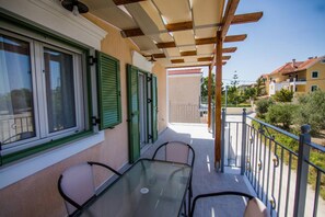 Ein Balkon mit Glastisch und Stühlen, einer Holz-Pergola und Blick auf benachbarte Gebäude.