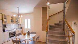 A modern kitchen with white cabinets, a dining table with chairs, and a staircase with a wooden handrail. - Villa Elpida at Minies (Kefalonia)